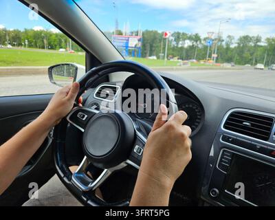 Person woman is driving a car with a steering wheel . The person is holding the steering wheel with both hands and he is in control of the vehicle Stock Photo