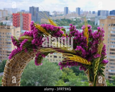 Wreath made of purple flowers and yellow wheat is displayed on a balcony. The flowers and wheat are arranged in a way that creates a sense of harmony and balance. The wreath is a beautiful Stock Photo