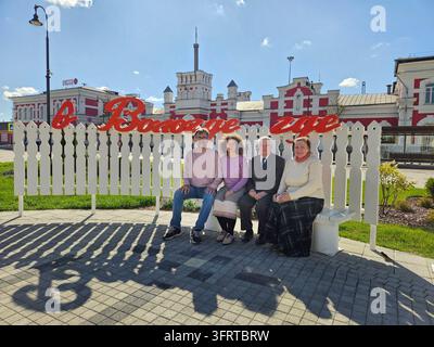 Group of four people sitting on a bench in front of a sign that says In Vologda where - Text from song Stock Photo