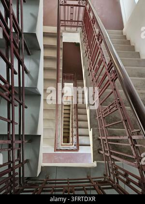 Spiral staircase with a red railing. The stairs are made of metal and are very narrow. The railing is made of iron and is very ornate Stock Photo