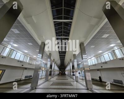 Empty station hall with tall columns and skylights. Ceiling panels and tiled floors reflect overhead lighting. Passenger benches line both sides of th Stock Photo