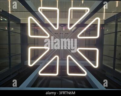 Neon sign glows brightly in modern glass enclosure. Geometric star pattern emits warm, inviting light. Design reflects symmetry through crisp, angular lines. Clean lines contrast with dark Stock Photo
