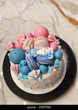 Colorful macarons adorn a decorated cake at gender party. Soft pastel hues create a sweet, festive look. Blue and pink macarons sit atop frosted cake. White cake base with blue and pink dot accents Stock Photo