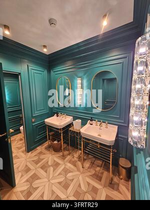 MOSCOW - JAN 15, 2026: Luxurious teal bathroom with elegant gold fixtures. Double sinks stand beneath mirrored oval frames. Tilework features a geometric pattern in neutral tones Stock Photo