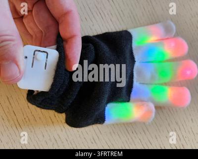 Hand holds glowing LED glove with colorful finger lights. Glove features black fabric with embedded lights. Each finger emits vibrant, shifting colored illumination Stock Photo