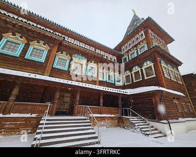 Snow falls gently on a traditional wooden building. Snow covers the steps and railings. Windows feature colorful, intricate frames. Tall tower with a golden spire stands above Stock Photo