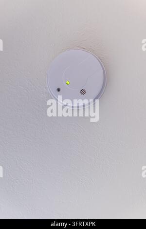 White circular smoke detector mounted on textured wall, featuring glowing green indicator light, compact design and ample negative space. Stock Photo