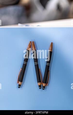 Three black ballpoint pens with rose gold accents and textured grips arranged on blue tabletop, photographed from above with soft natural lighting. Stock Photo