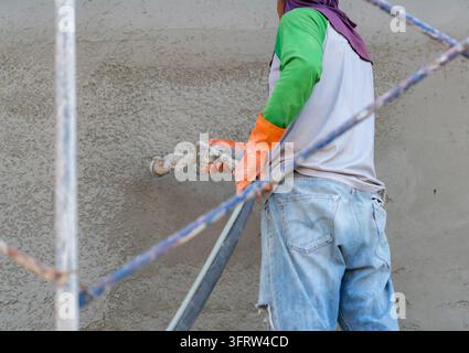 Builder on scaffolding spraying textured plaster onto a wall surface with specialized equipment during home renovation and construction work. Stock Photo