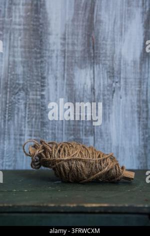A rough coil of brown rope rests on a dark green tabletop against a weathered blue wooden wall. Stock Photo