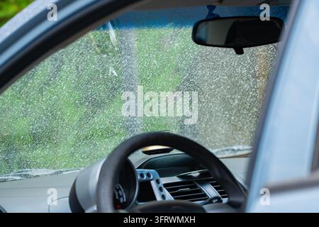 Inside view of a car through a heavily dirty windshield covered with dust and dried spots, showing the steering wheel and dashboard, illustrating car Stock Photo