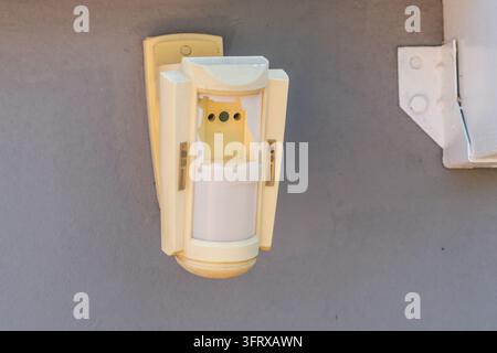 Damaged motion sensor with exposed components is mounted on a gray wall. Stock Photo