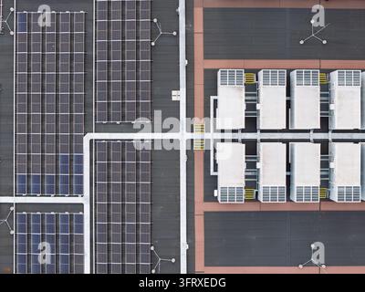Aerial view showing rows of solar panels alongside industrial cooling units on the roof of a large Data Center facility during a bright day Stock Photo