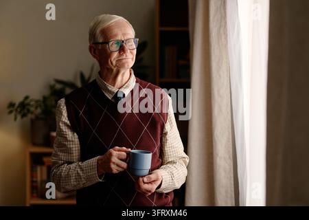 Senior Man Holding Coffee Cup Looking through Window at Home Stock Photo
