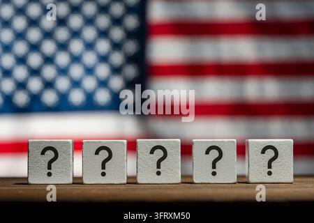 Question marks on wooden blocks with American flag background, close up. Row white cubes with black question marks. Conceptual image for American poli Stock Photo