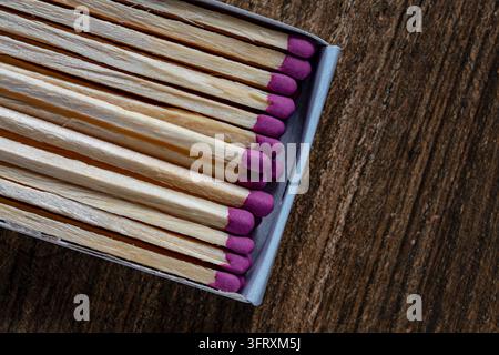 Matches with pink heads in cardboard box close up. Top view of wooden matches with purple sulfur heads inside a matchbox. Row of matchsticks on dark b Stock Photo