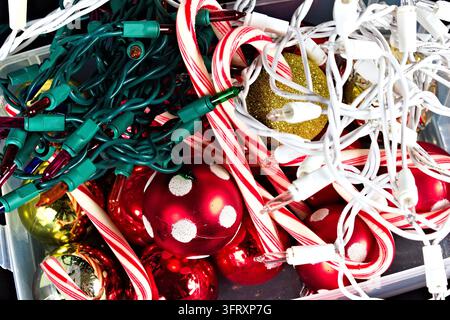 Red ornaments with white dots, striped candy canes, gold glitter and green and white Christmas lights fill a crowded holiday decoration box. Stock Photo