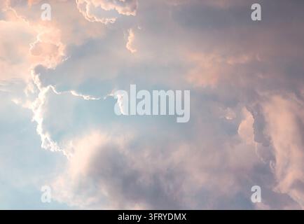 A mesmerizing expanse of dramatic, billowy cumulus clouds bathed in gentle, ethereal sunlight. The image captures a rich interplay of light and shadow Stock Photo