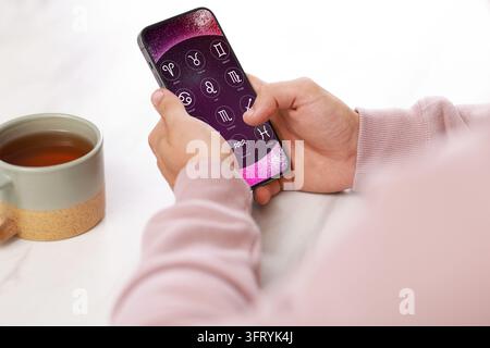 Man using astrology app on his smartphone at white table with cup of tea, closeup Stock Photo