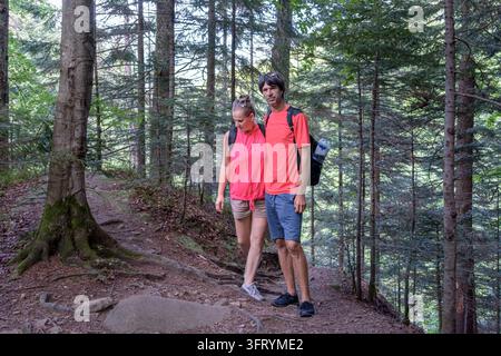 Couple hikers with backpacks standing and embracing on forest trail on way to Maniava Waterfall, Carpathians, Ukraine. Man and woman together Stock Photo