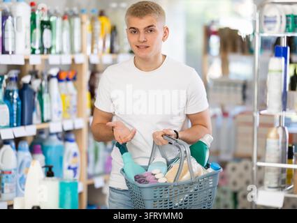 Guy selects various household cleaning products for cleaning the house with full basket of various purchases Stock Photo