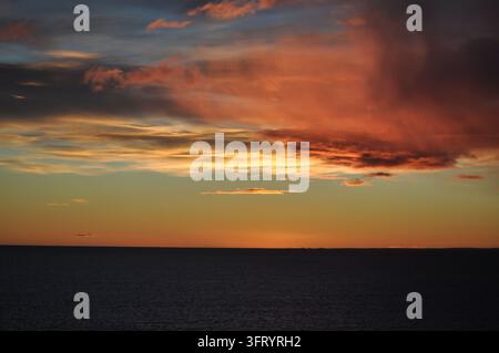 Fiery Red and Orange Sunset Clouds Over the Dark Ocean Horizon Stock Photo