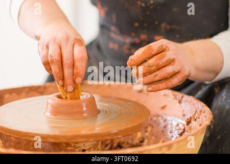 Potter hands are actively shaping and smoothing a piece of wet clay on a spinning pottery wheel, demonstrating traditional craftsmanship and artistic Stock Photo
