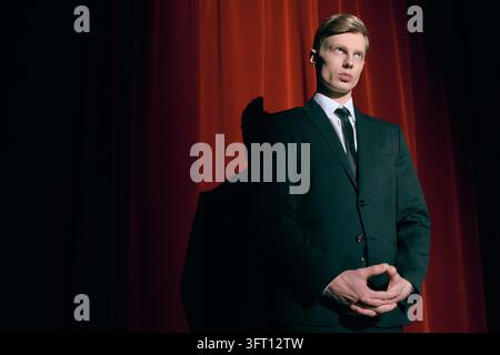 A stylish young man stands poised near a red curtain, exuding mystery in twin peaks aesthetic studio Stock Photo