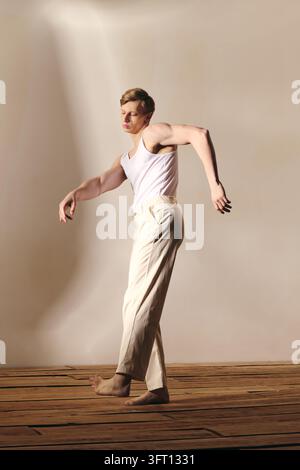 A young blonde male dancer displays expressive movement in a studio setting Stock Photo