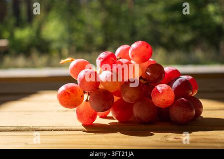 A bunch of red grapes lies on a wooden table on a sunny day, front view. Stock Photo