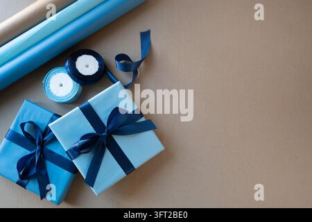 Two blue gift boxes with navy satin bows and wrapping supplies arranged on kraft paper. Flat lay with large copy space for holiday promotion, birthday Stock Photo