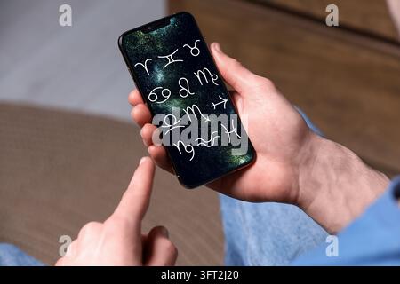Man using astrology app on his smartphone indoors, closeup Stock Photo