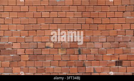 Red hollow clay brick wall of a house under construction, unplastered with rough mortar joints, a full frame brick wall texture Stock Photo