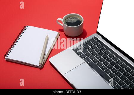 Laptop with blank screen, coffee and notebook with pen on red background Stock Photo