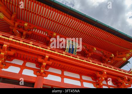 Kyoto, Japan - Sep 23 2024, panoramic view from below of the red facade of the Fushimi Inari Temple building with a roof cornice, with a cloudy sky in the background, Kyoto, Japan Stock Photo