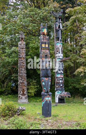 Vancouver, Canada - September 7, 2026: Vertical perspective of three carved and painted First Nations cedar totem poles standing in a lush clearing at Stock Photo