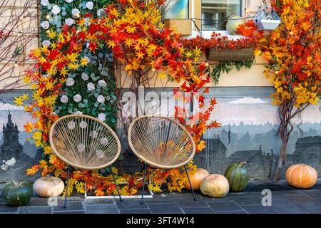 Cozy autumn outdoor seating area with two wicker chairs surrounded by colorful fall foliage, pumpkins and vibrant maple leaves decorating a charming Stock Photo