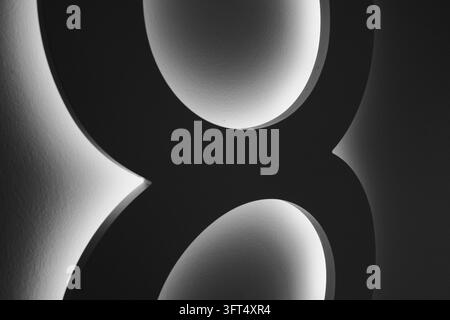 Black curved sections of a large wall numeral fill the horizontal frame, with white light outlining the inner openings. Tight cropping turns functiona Stock Photo