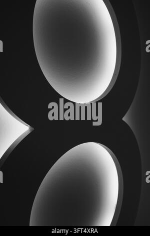 An extreme vertical crop isolates the thick black strokes and softly glowing interiors of two rounded loops. The wall-mounted numeral becomes an abstr Stock Photo