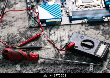 Close-up of a computer motherboard repair process with a digital multimeter, test probes, and a screwdriver on a textured surface. Perfect for electro Stock Photo