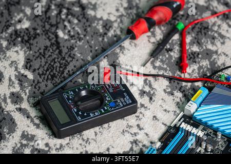 Close-up of a computer motherboard repair process with a digital multimeter, test probes, and a screwdriver on a textured surface. Perfect for electro Stock Photo