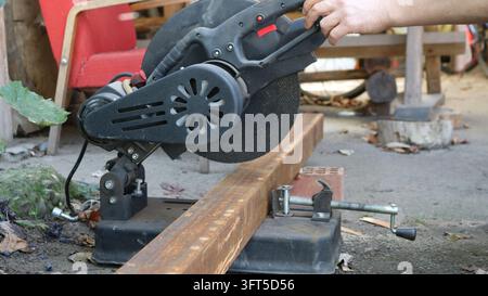 A craftsman at work with a miter saw. A section of structural steel tubing, showing traces of rust, is positioned on the equipment's platform Stock Photo