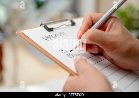Close up of a person holding a pen and checking off items on a checklist clipboard, business planning concept. Stock Photo