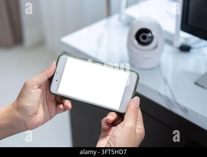 Woman holding a smart mobile phone with isolate screen and blurred images of cctv cameras installed in apartment background. Close up and copy space Stock Photo