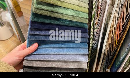 Close-up of customer hand selecting colorful upholstery fabric samples in different shades and textures at furniture showroom Stock Photo