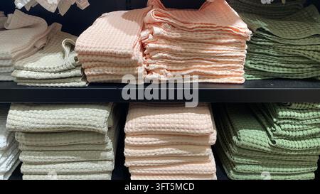 Folded waffle weave bath towels in white, peach and sage green colors stacked on black shelves at home textile store Stock Photo