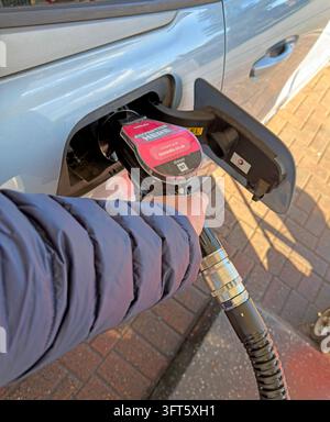 Hand holding diesel-pump nozzle while refuelling a silver car at a filling station. Stock Photo