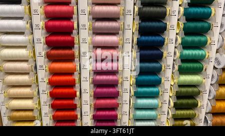 Assorted colorful sewing thread spools in different shades arranged on display racks at craft supply store Stock Photo