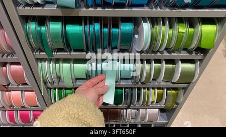 Close-up of customer hand selecting mint green satin ribbon from assorted colorful ribbon spools displayed on shelves at craft supply store Stock Photo