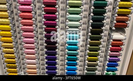 Assorted colorful sewing thread spools in different shades arranged on display racks at craft supply store Stock Photo